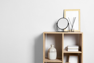 Photo of Stylish mirror, reed diffuser and picture frame on shelf near light wall, space for text. Interior design