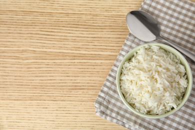 Photo of Bowl with tasty cooked rice on wooden table, flat lay. Space for text