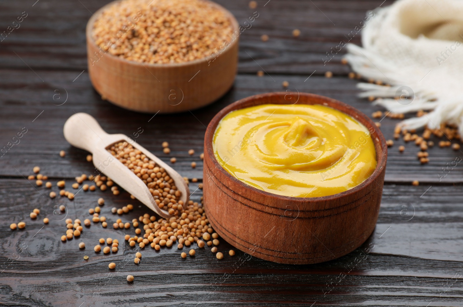 Photo of Delicious mustard and seeds on dark wooden table, closeup