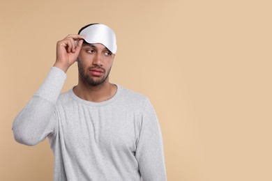 Photo of Tired man with sleep mask on beige background, space for text. Insomnia problem