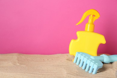 Photo of Suntan product and plastic beach toy on sand against pink background. Space for text