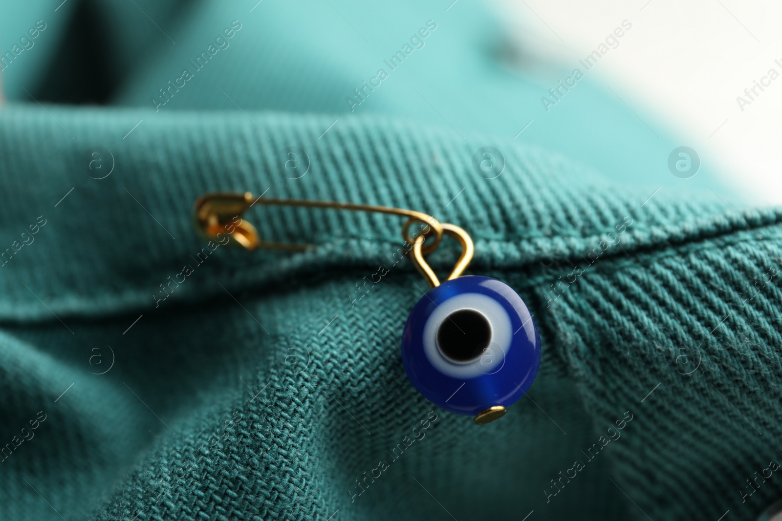 Photo of Evil eye safety pin on denim clothing, closeup