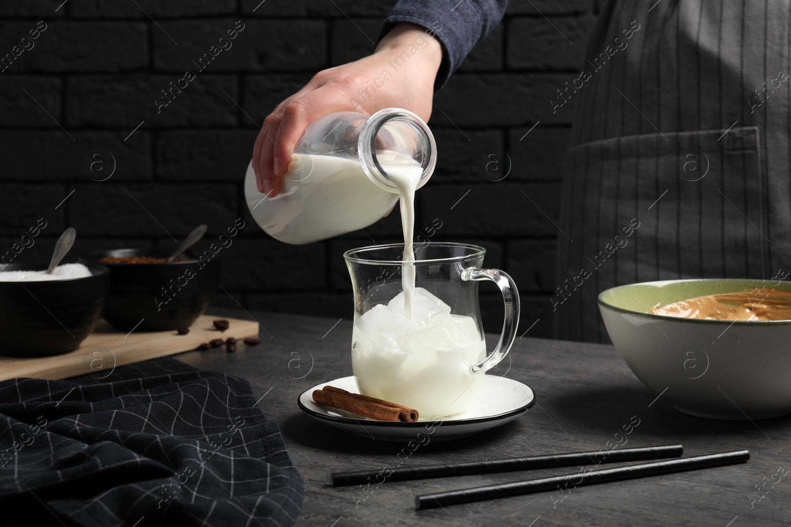 Photo of Woman pouring milk into glass at grey table, closeup