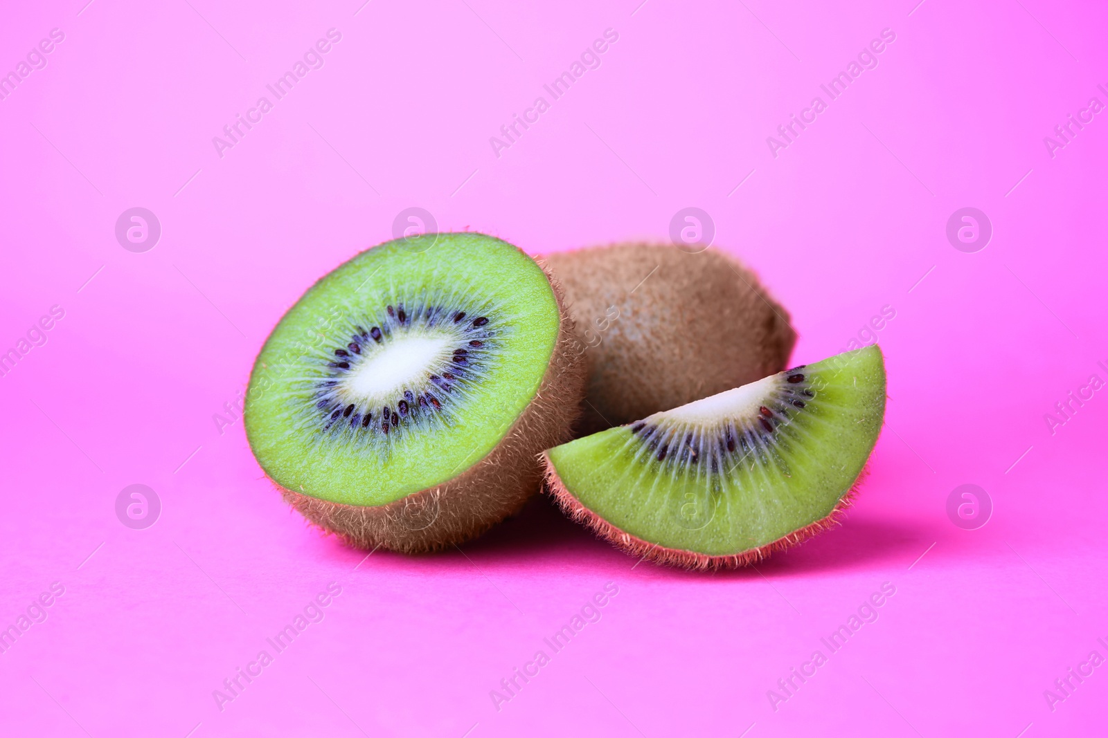 Photo of Whole and cut fresh kiwis on pink background