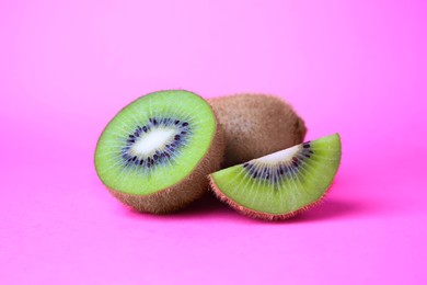 Whole and cut fresh kiwis on pink background