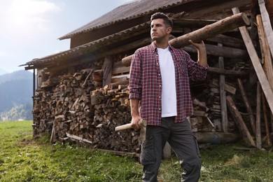 Man with ax and log near wood pile outdoors