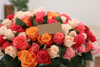 Photo of Bouquet of beautiful roses with blank card indoors, closeup