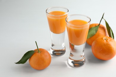 Photo of Tasty tangerine liqueur in shot glasses and fresh fruits on white table. Space for text