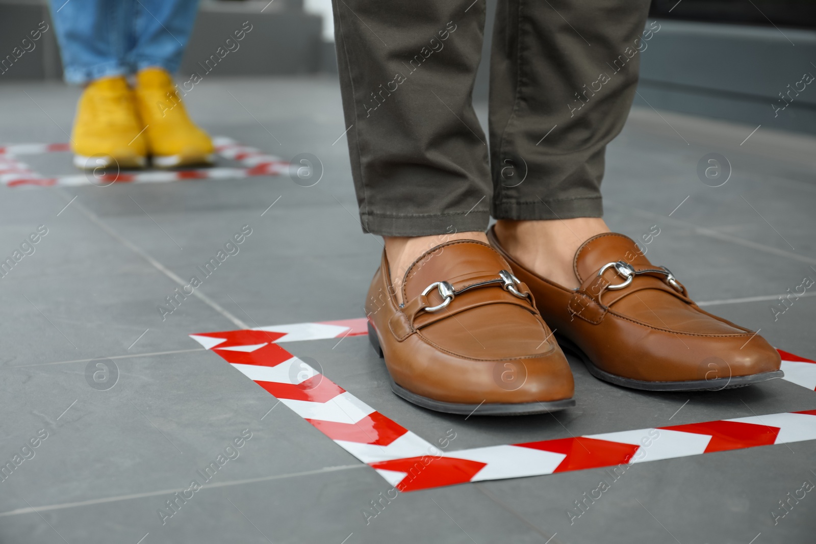 Photo of People standing on taped floor markings for social distance, closeup. Coronavirus pandemic