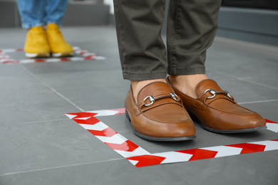 People standing on taped floor markings for social distance, closeup. Coronavirus pandemic