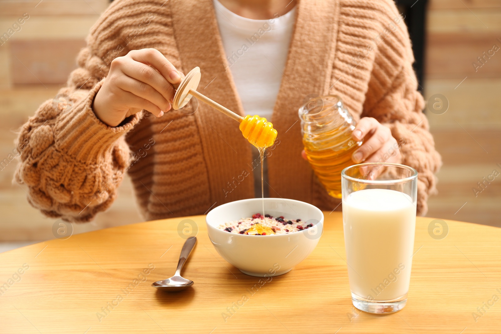 Photo of Woman adding honey to oatmeal at wooden table, closeup