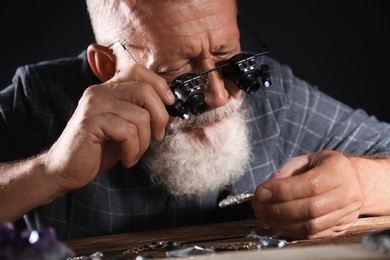 Photo of Male jeweler evaluating diamond brooch in workshop, closeup view