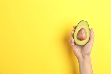 Photo of Woman holding ripe cut avocado on color background