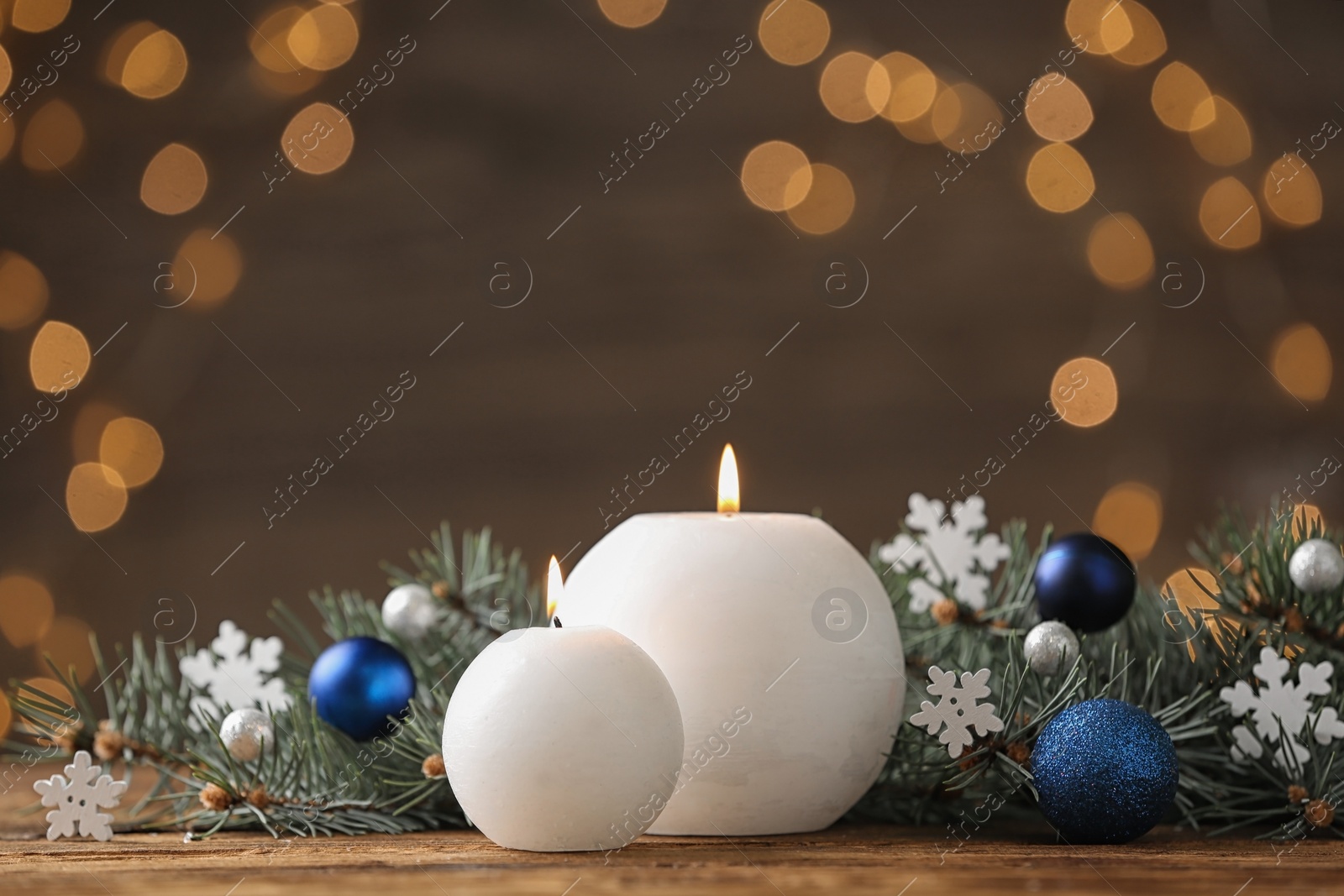 Photo of Candles and Christmas decor on wooden table against blurred festive lights, space for text. Winter holiday