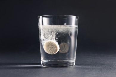 Effervescent pill dissolving in glass of water on grey table