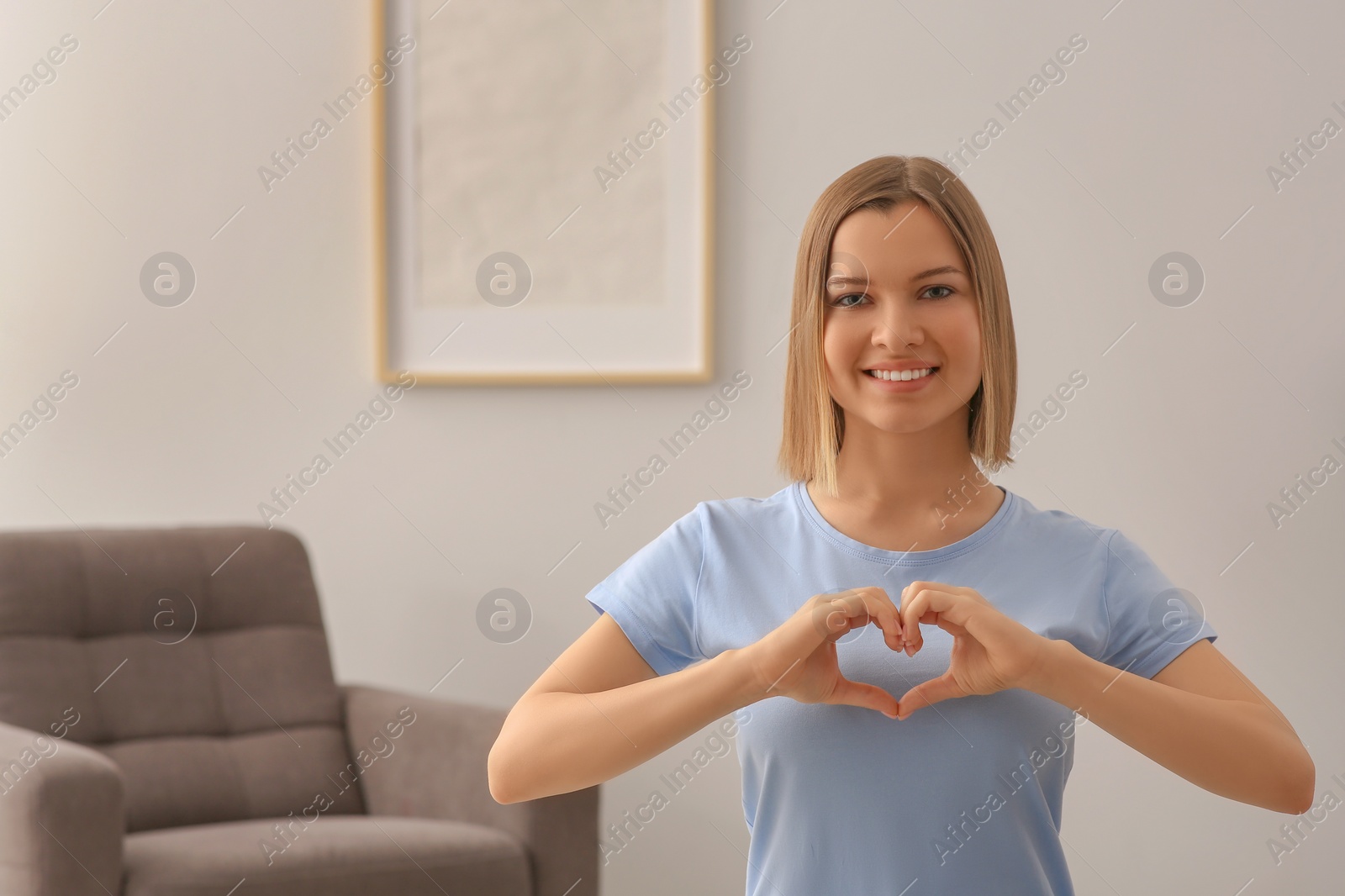 Photo of Young woman making heart with hands indoors, space for text. Volunteer concept