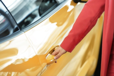 Photo of Young woman opening door of new car, closeup