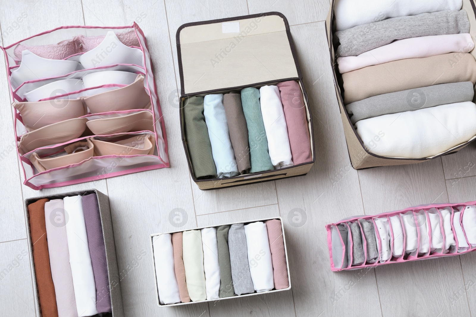 Photo of Different organizers with folded clothes and underwear on white wooden background, flat lay. Vertical storage