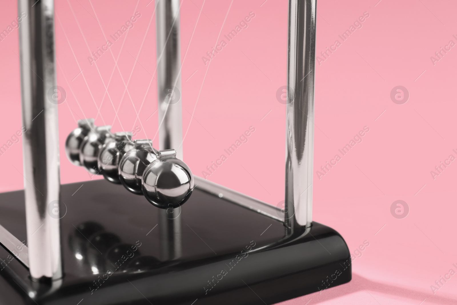 Photo of Newton's cradle on pink background, closeup. Physics law of energy conservation