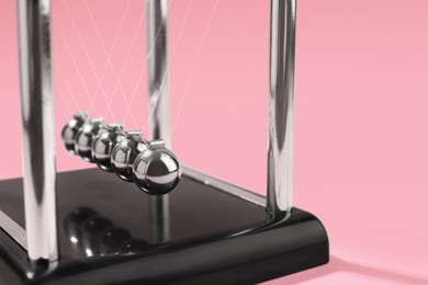 Newton's cradle on pink background, closeup. Physics law of energy conservation