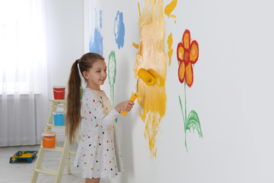 Little child painting wall with roller brush indoors