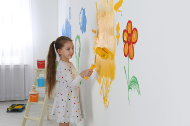 Photo of Little child painting wall with roller brush indoors