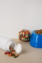 Bottle with vitamins, toy and dry pet food in bowl on beige table