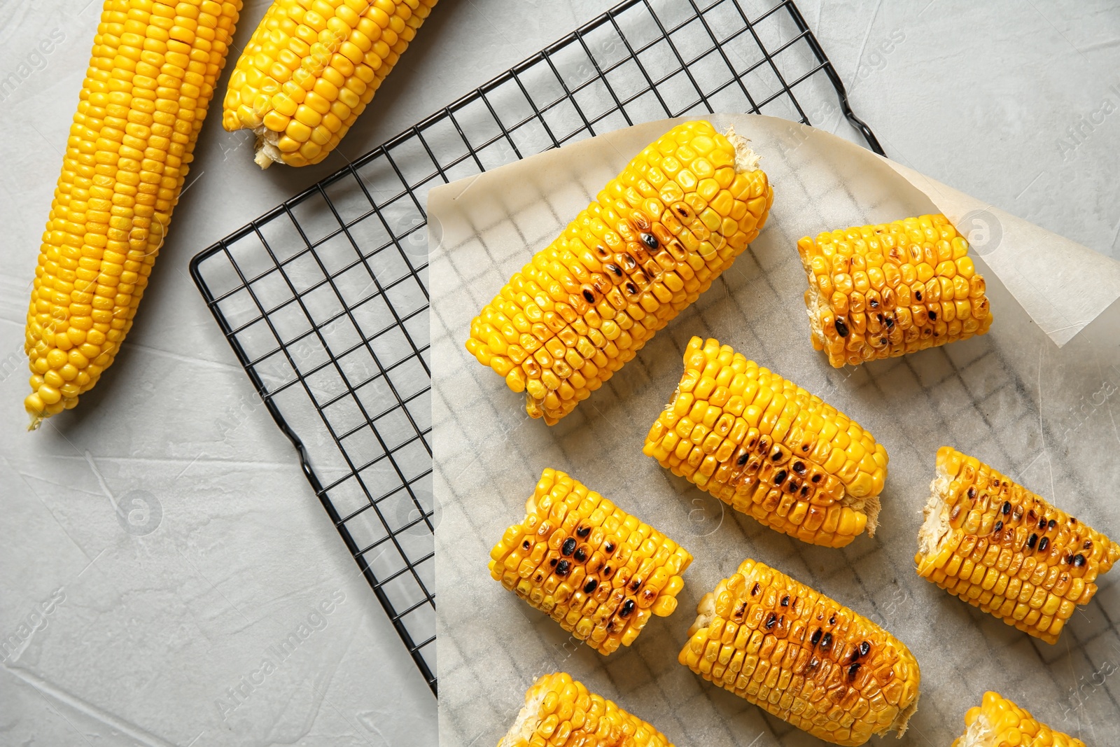 Photo of Cooling rack with grilled corn cobs on light background, top view