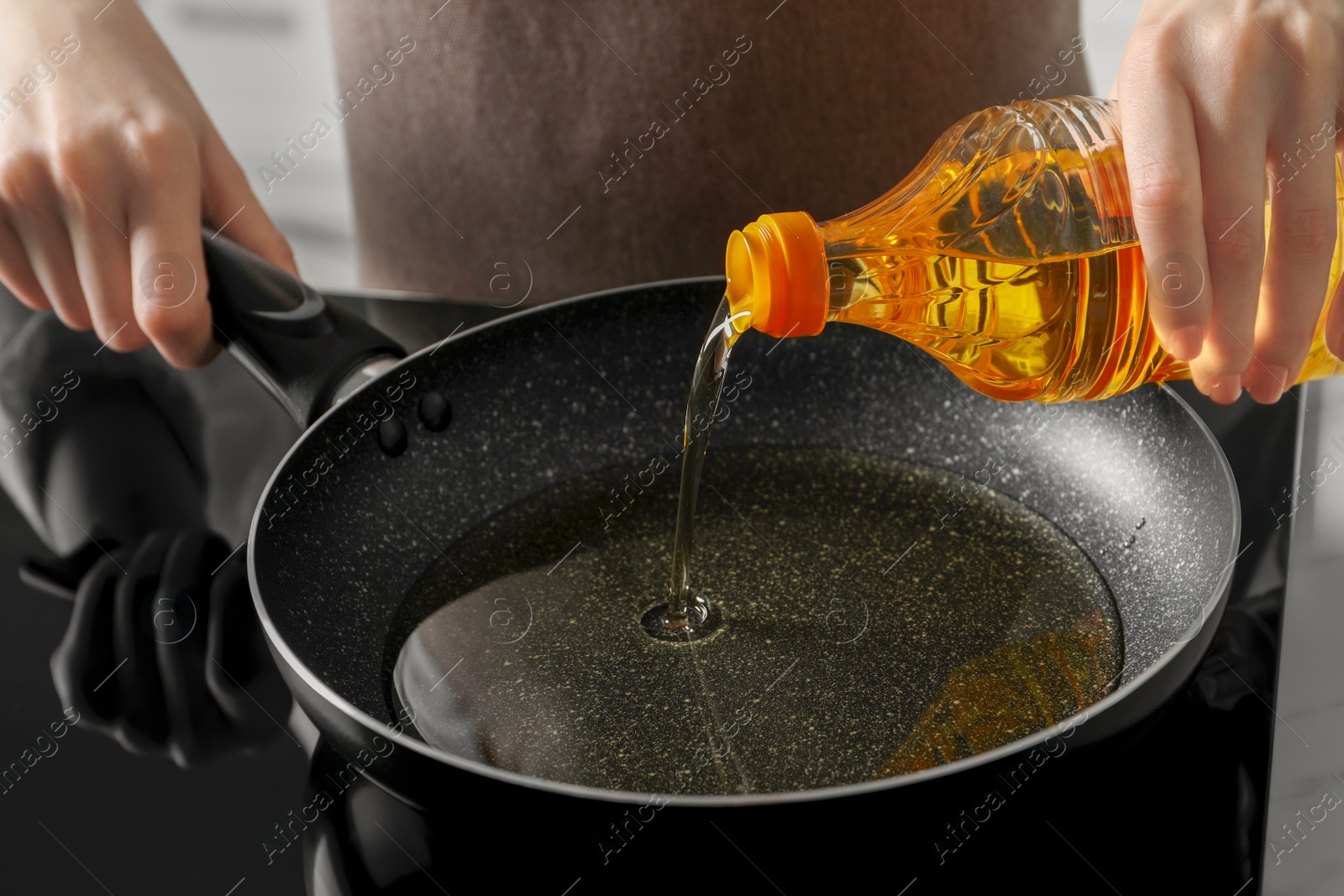 Photo of Woman pouring cooking oil from bottle into frying pan on stove, closeup