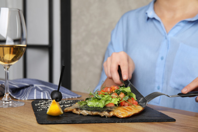 Photo of Woman eating delicious grilled fish with vegetables at wooden table, closeup