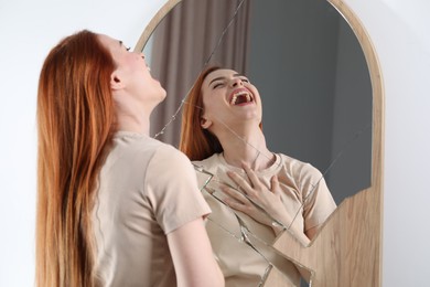 Mental problems. Young woman laughing near broken mirror indoors