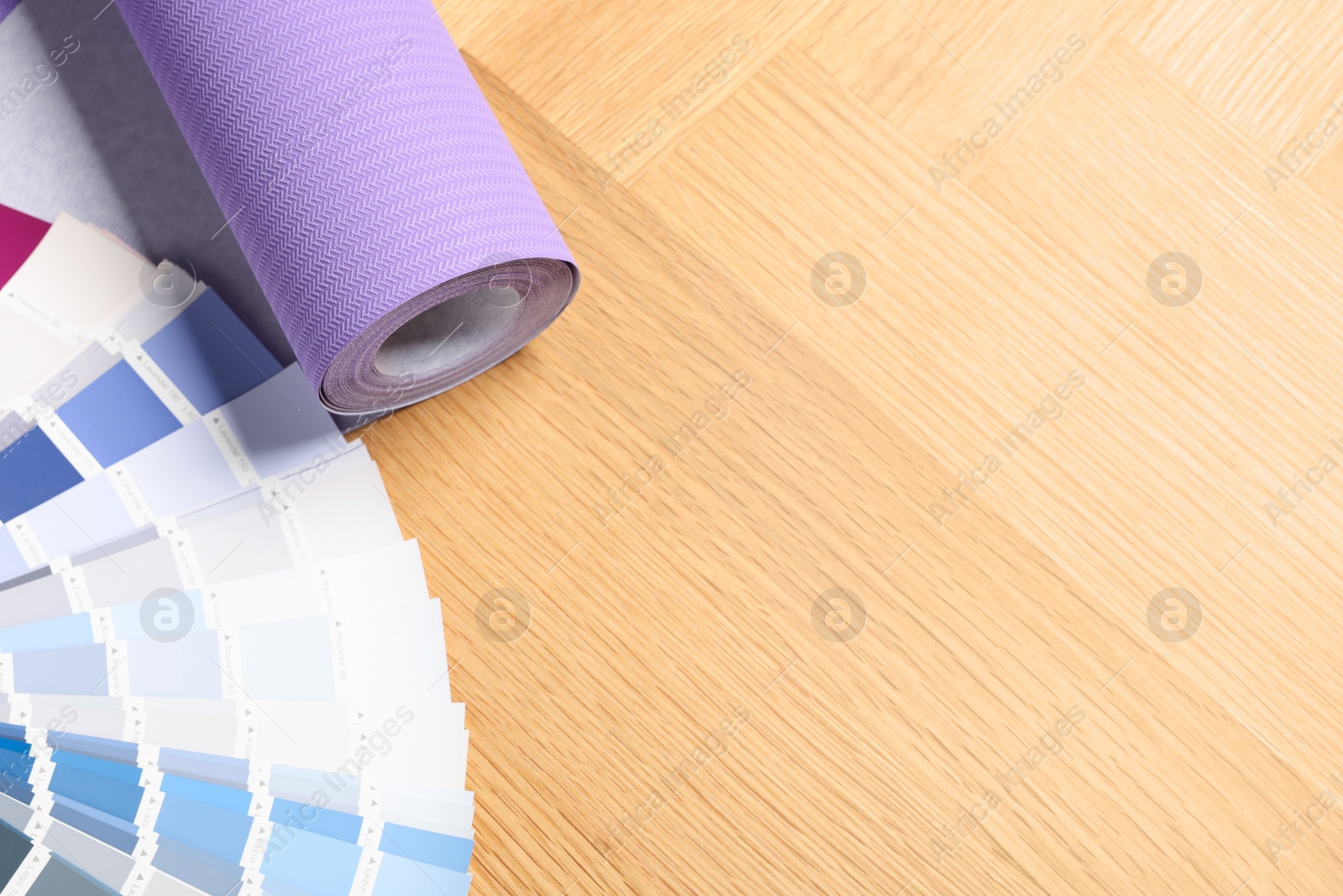 Photo of Violet wallpaper roll and color palette samples on wooden table, top view. Space for text