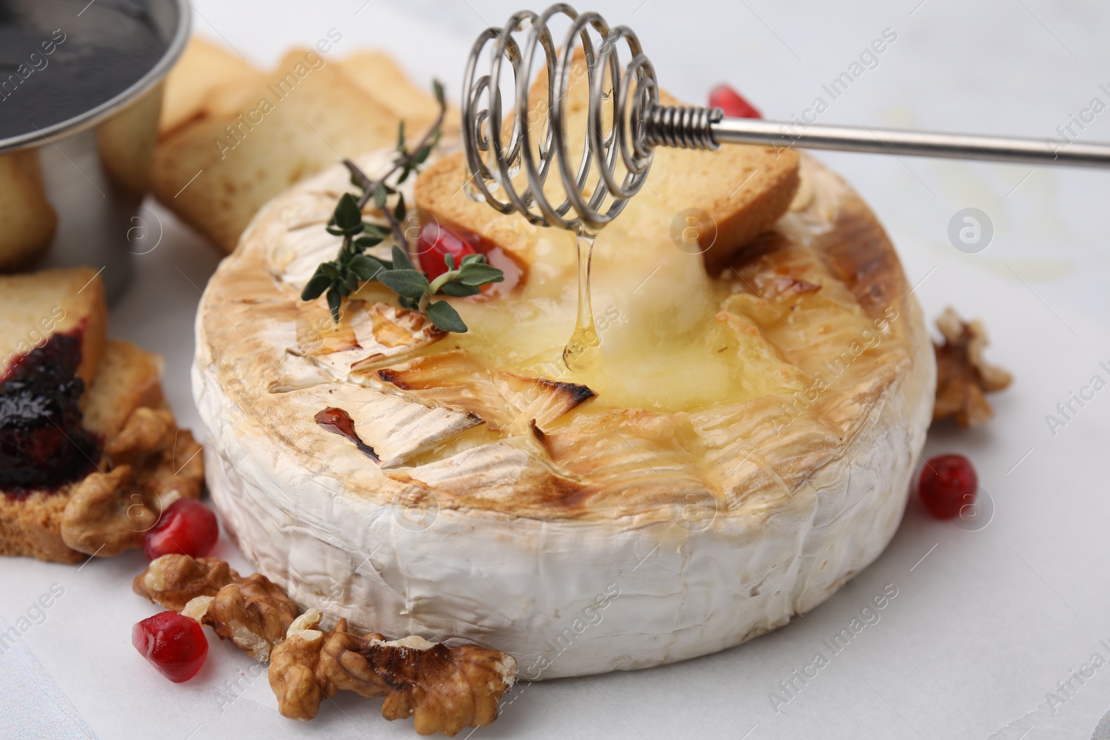 Photo of Pouring honey onto tasty baked camembert with thyme on white table, closeup