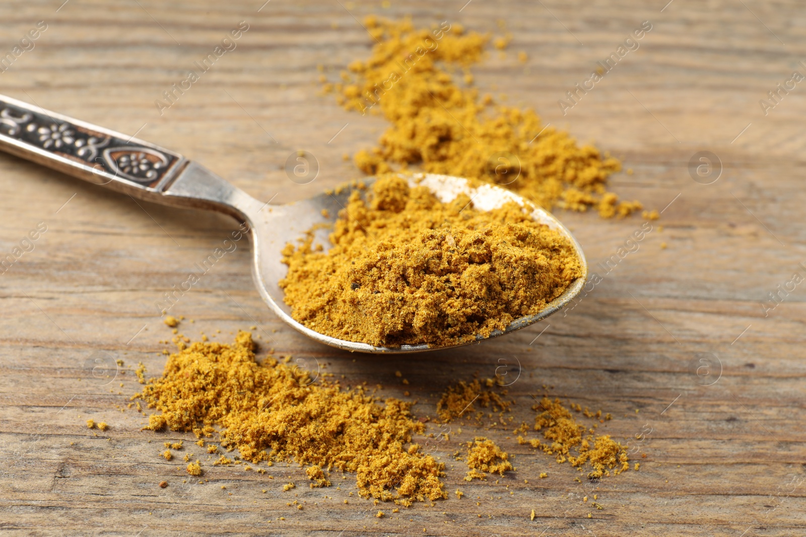 Photo of Spoon with dry curry powder on wooden table, closeup