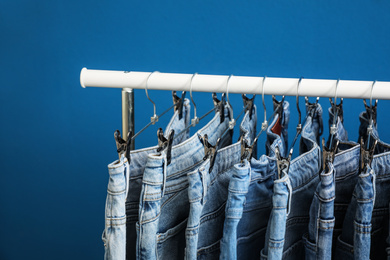Photo of Rack with stylish jeans on blue background, closeup