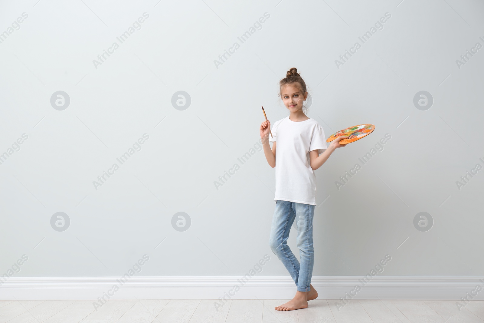 Photo of Little girl with brush and paint palette near light wall indoors. Space for text