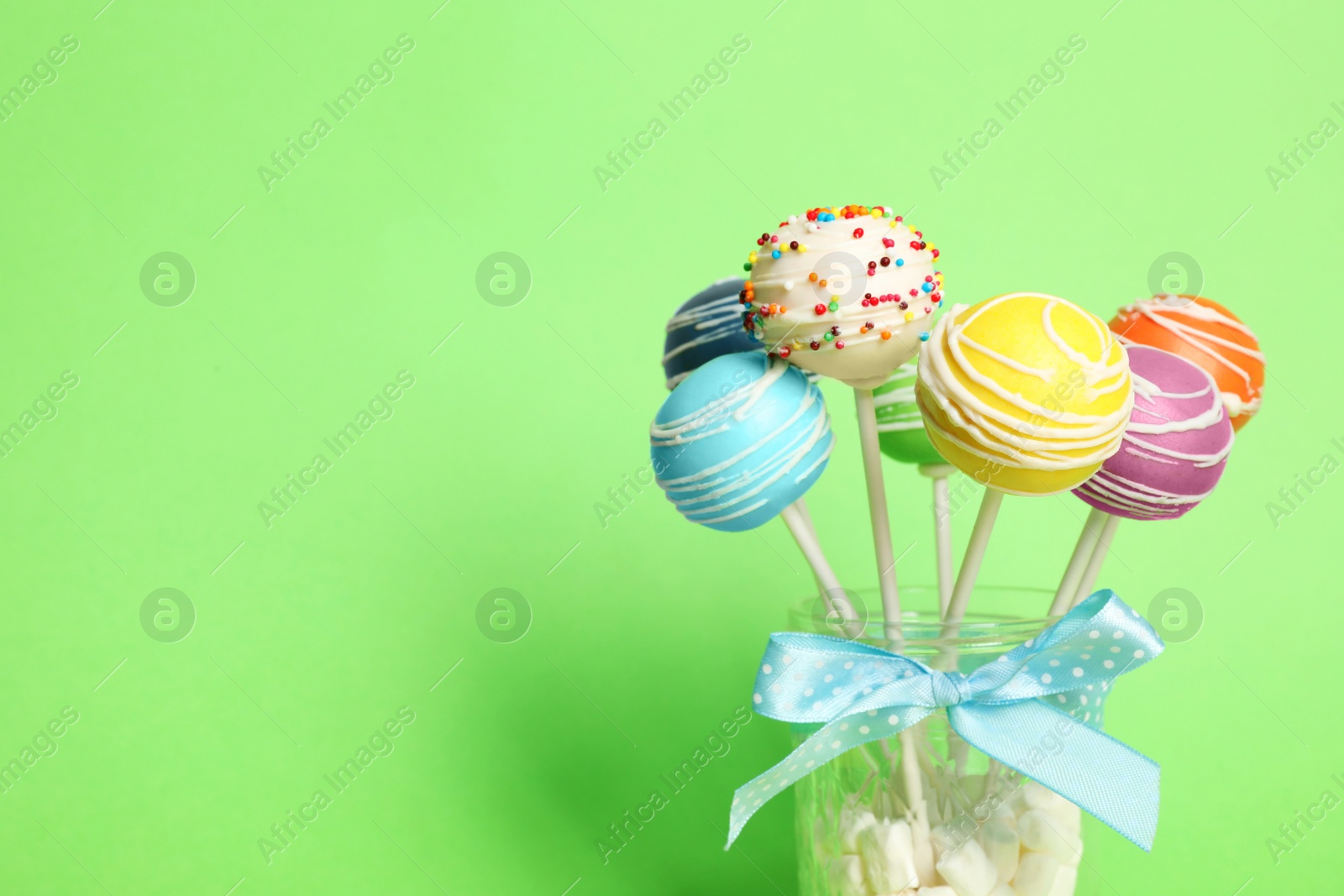 Photo of Delicious cake pops in jar full of marshmallows on color background. Space for text