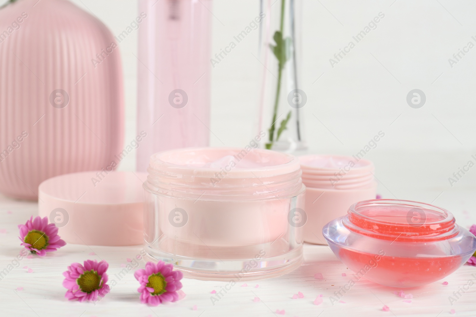 Photo of Homemade cosmetic products and beautiful flowers on white wooden table, closeup