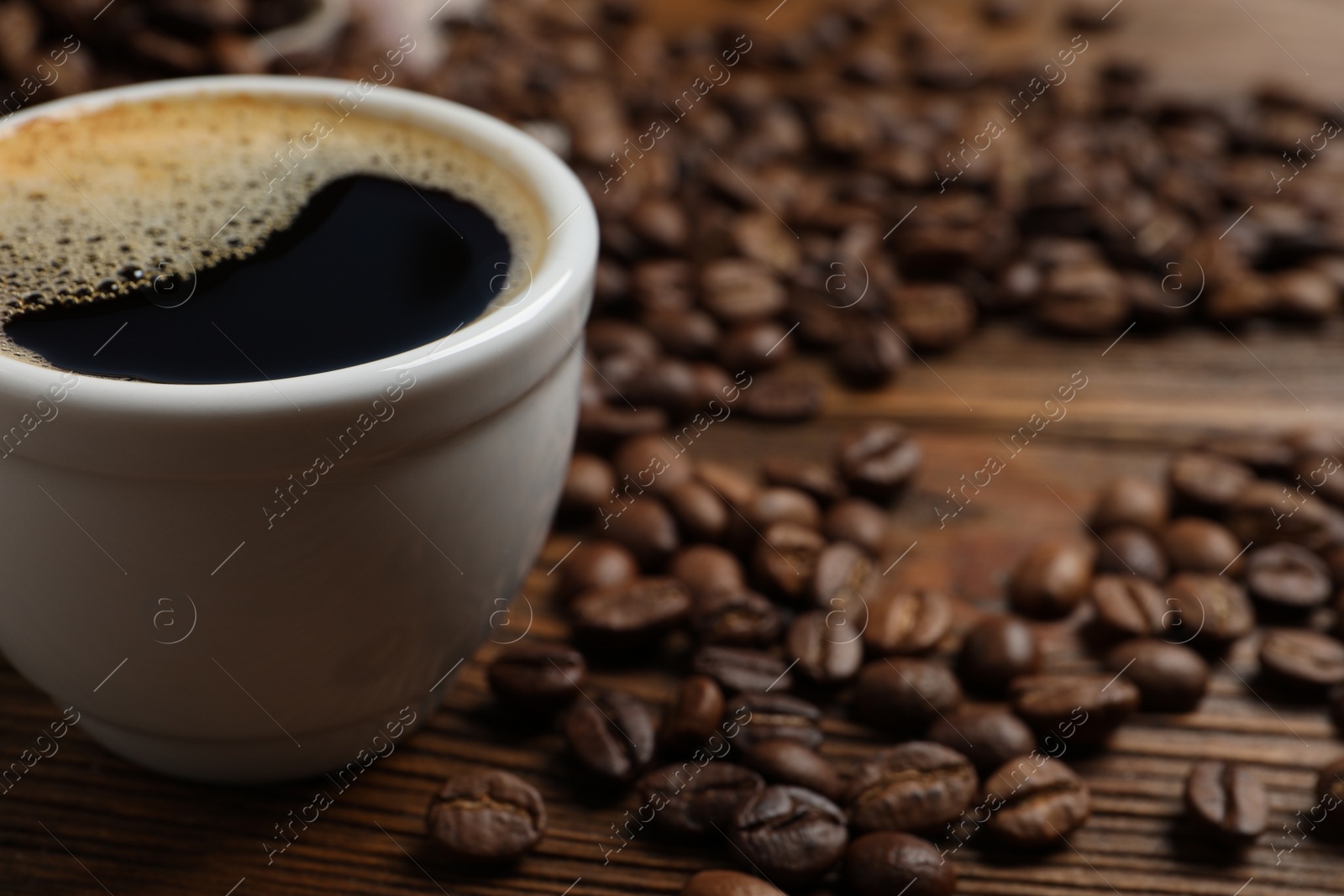 Photo of Cup of aromatic hot coffee and beans on wooden table, closeup. Space for text