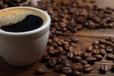 Cup of aromatic hot coffee and beans on wooden table, closeup. Space for text