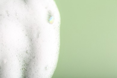 White fluffy foam on green background, top view. Space for text