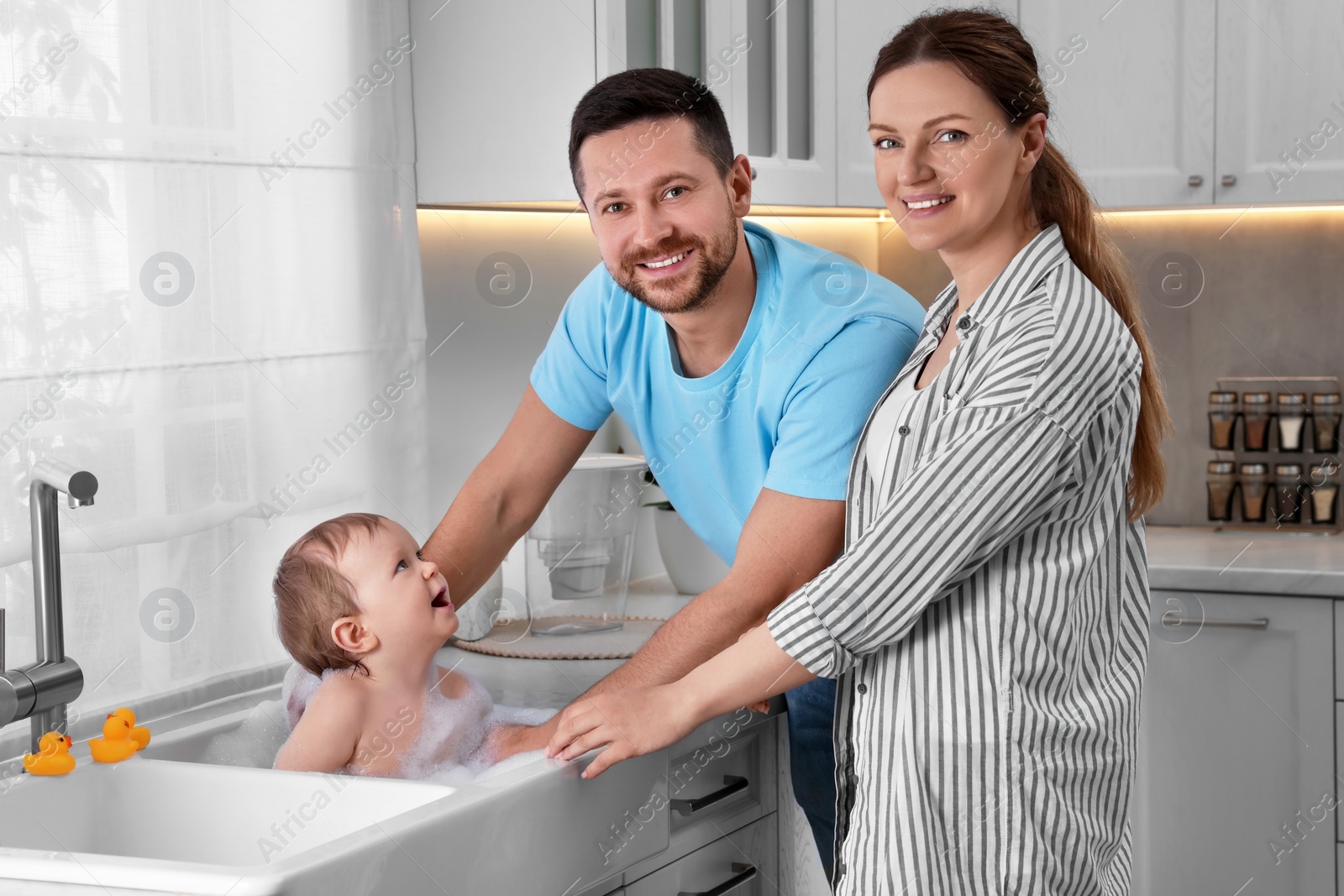 Photo of Father and mother washing their little baby in sink at home