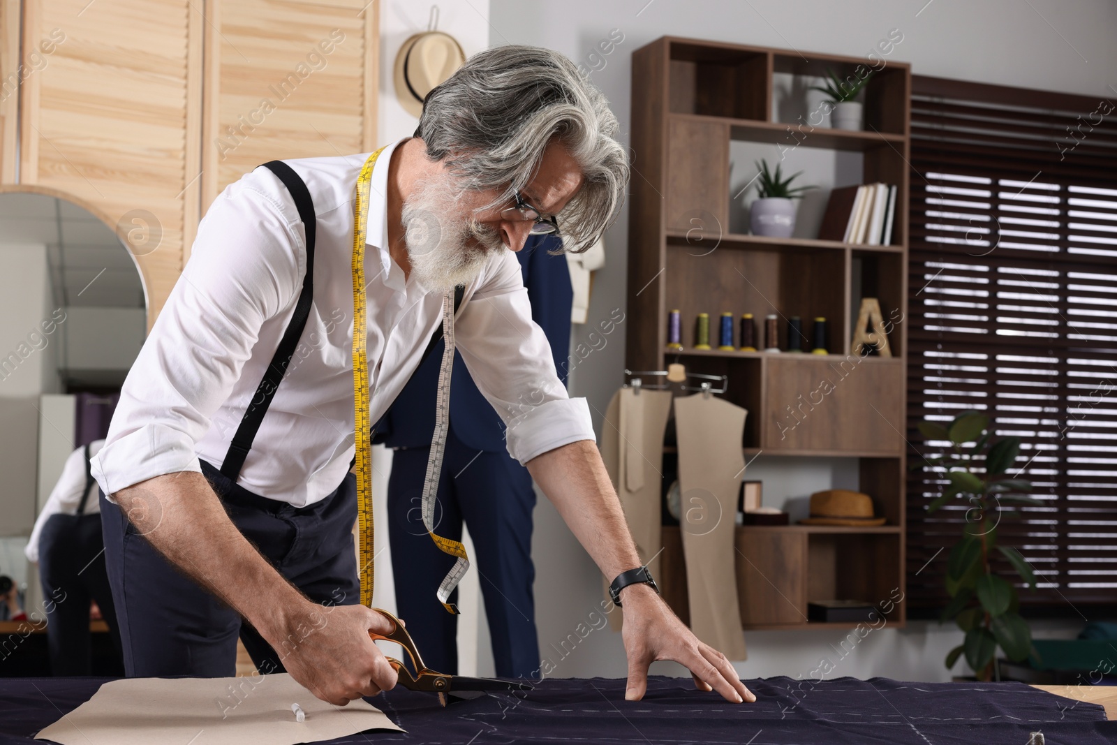 Photo of Professional tailor cutting fabric by following chalked sewing pattern at table in workshop, space for text