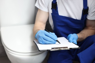 Plumber writing results of examining toilet bowl, closeup