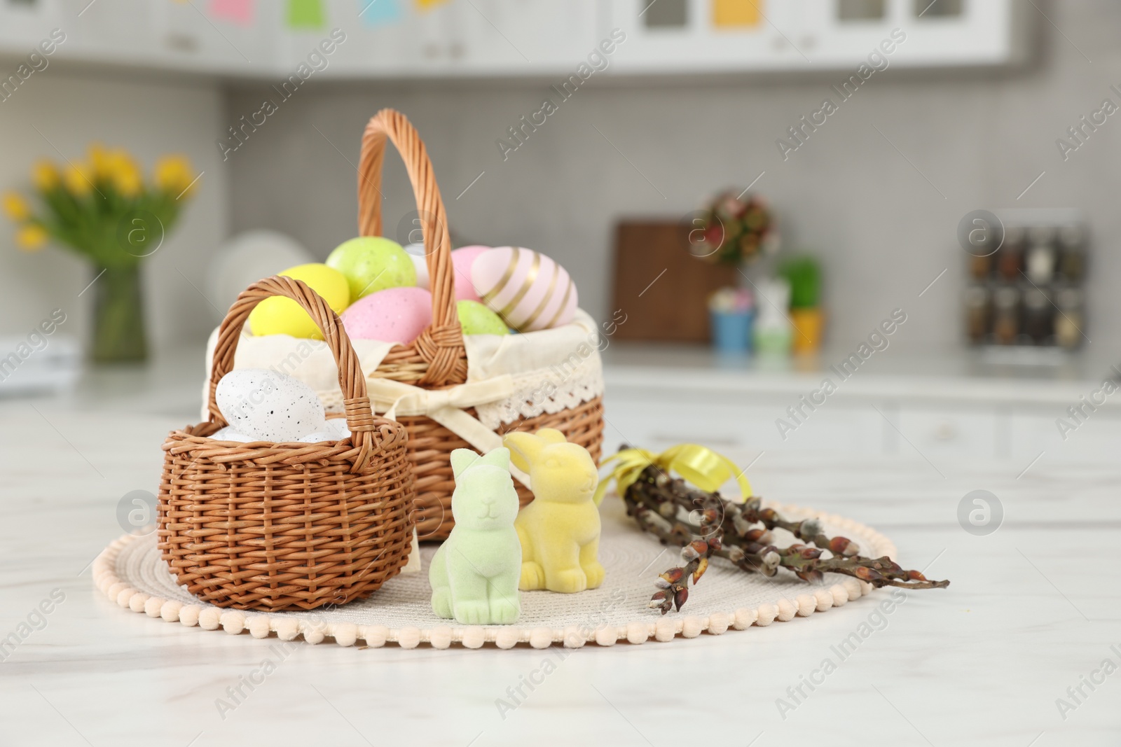 Photo of Wicker baskets with Easter eggs and willow twigs at white marble table in kitchen