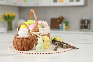 Wicker baskets with Easter eggs and willow twigs at white marble table in kitchen