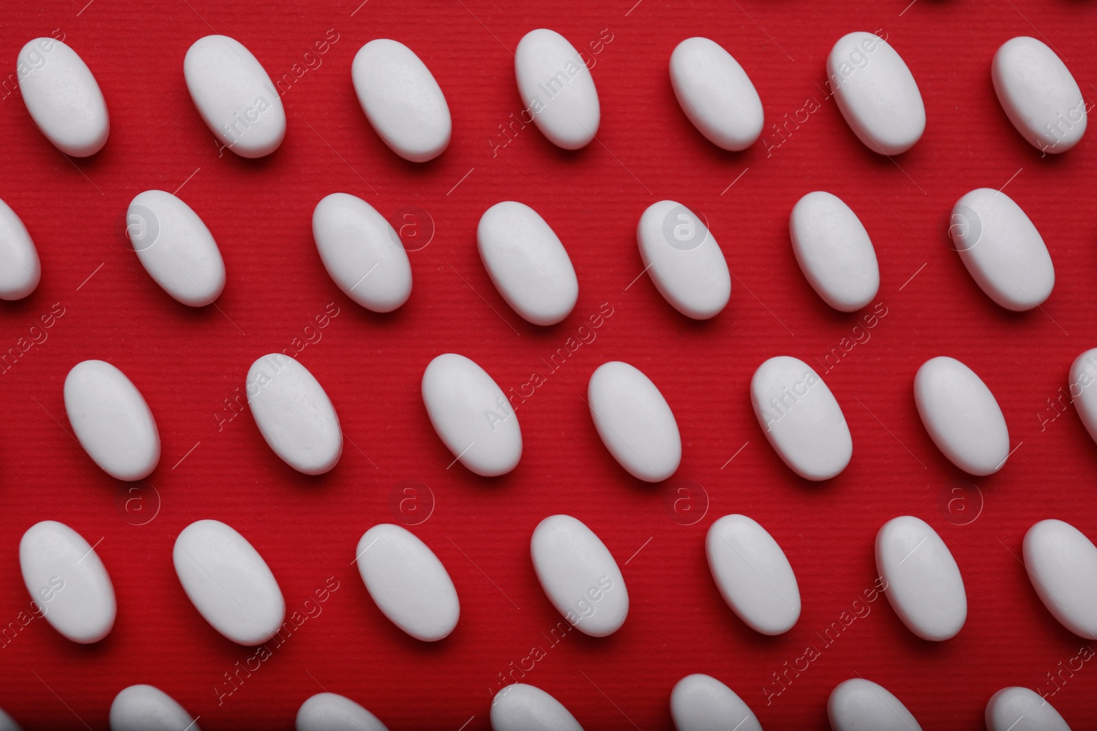 Photo of Many white dragee candies on red background, flat lay