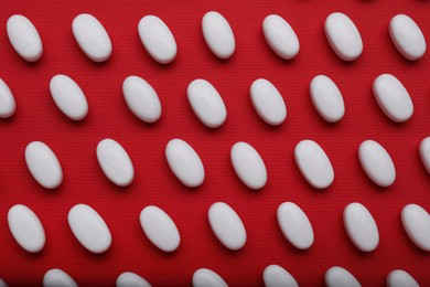 Photo of Many white dragee candies on red background, flat lay