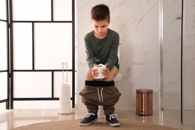 Photo of Boy with paper suffering from hemorrhoid on toilet bowl in rest room