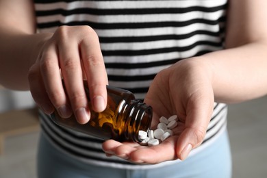 Photo of Woman pouring pills from bottle on blurred background, closeup